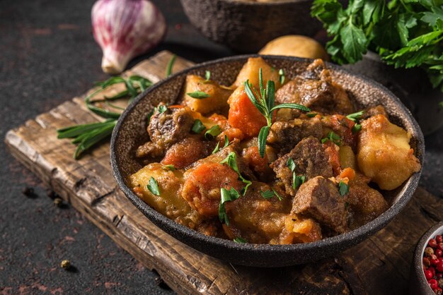 Irish stew made with beef meat, potatoes, carrots and herbs in a plate on black surface