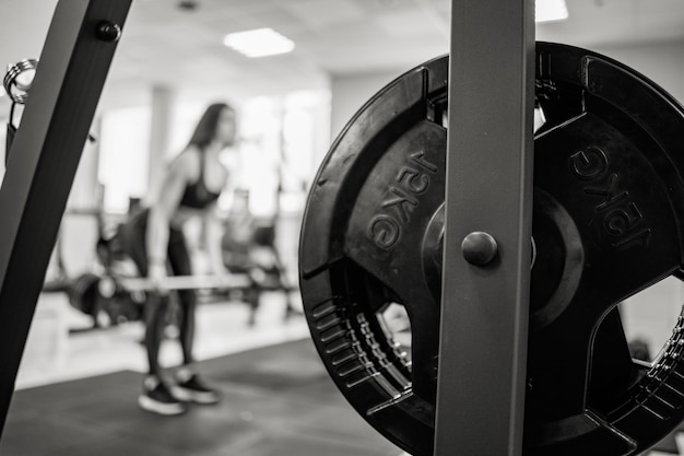 Photo iron barbell disk on the background of a woman training in the gym fifteen kg on the barbell disk closeup black and white photo