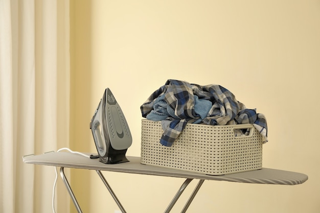 Iron and basket with clothes on ironing board