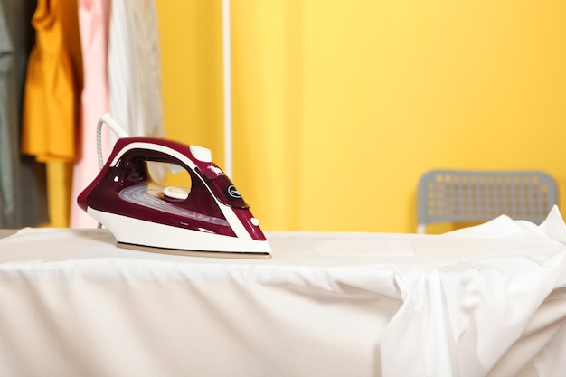 Iron and a clothes on an ironing board on a colored background