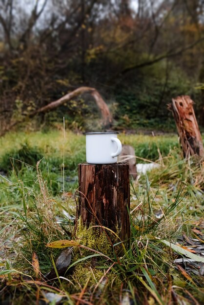 Photo iron mug stands on a stump in the forest. steam rises from the hot drink.
