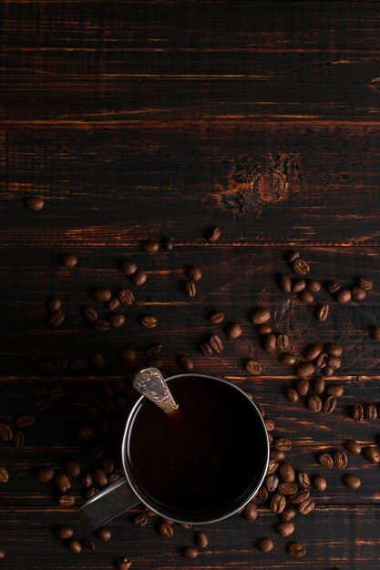 Foto rivesta di ferro la tazza con caffè nero e chicchi di caffè su una tavola di legno. copyspace.