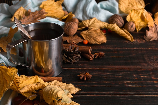 Iron mug with black coffee, spices, on a background of a scarf, dry leaves on a wooden table. Autumn mood, a warming drink. copyspace.