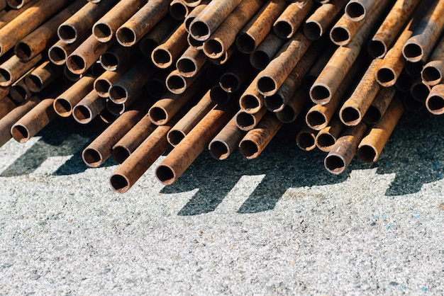 Iron pipes for gasification or water supply lie in pile on concrete outside on street on summer day Background