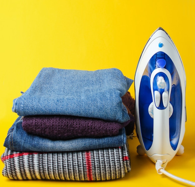 Iron and stack of clothes on yellow table