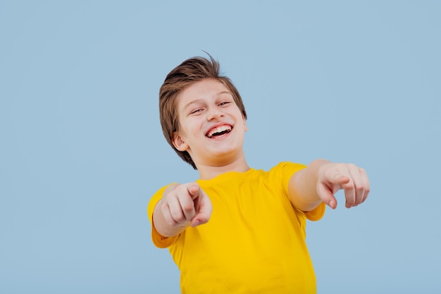 Ironically boy pointing at camera,in yellow t-shirt isolated on blue