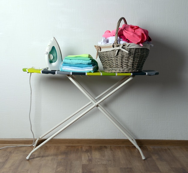 Ironing board with laundry on light background