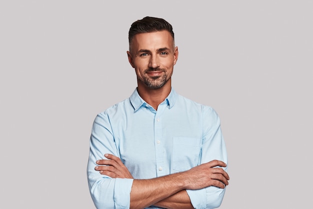 Irresistible man. Charming young man looking at camera and smiling while standing against grey background