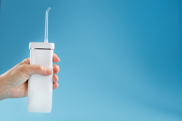 Irrigator in hand for cleaning the mouth on a blue surface