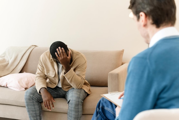 An irritated African American emotionally talks about problems to a psychologist at a session a confused unhappy young man undergoes therapy with a psychiatrist