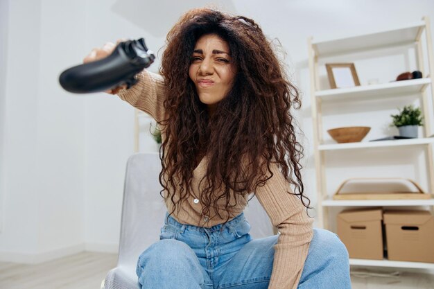 Irritated angry pretty tanned curly latin lady lose game throw\
joystick gamepad at camera sit on chair in home modern interior\
copy space mockup banner concept gamer people emotions concept