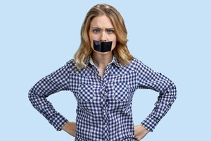 Irritated angry young woman with mouth covered with tape