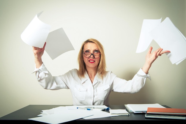 Irritated businesswoman with tousled hair throwing documents at desk against gray background