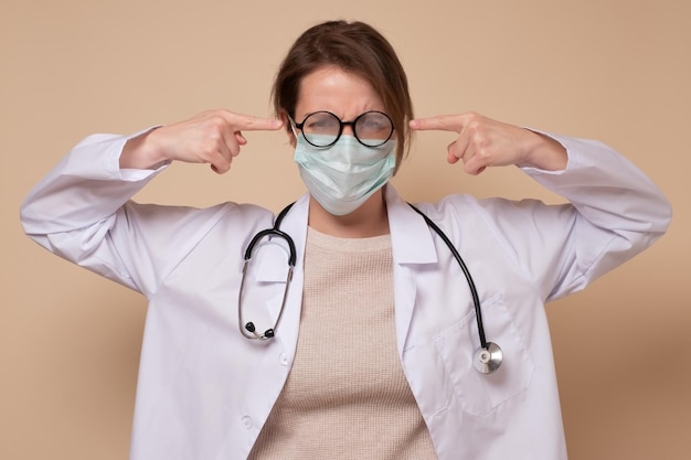 의료용 마스크를 쓴 성난 의사 여성은 귀를 막고 소음에 대해 불평하고 불쾌한 대화를 무시합니다. 부정적인 감정 개념입니다.