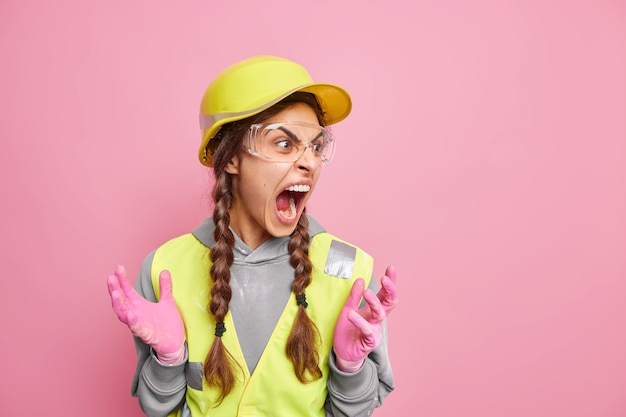 Irritated female contractor has two pigtails screams loudly expresses negative emotions 