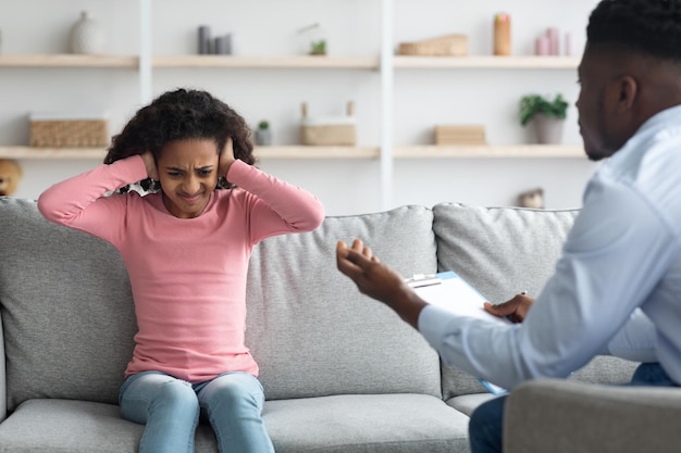 Irritated girl covering her ears while having conversation with psychotherapist