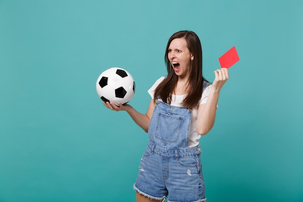 Irritated shocked young girl football fan support team with soccer ball, red card propose player retire from field isolated on blue turquoise background. People emotions, sport family leisure concept.