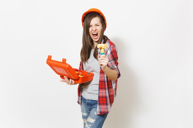 Irritated woman in protective hardhat holding opened case with instruments or toolbox and toy hammer and screaming isolated on white background. Instruments for renovation room. Repair home concept.