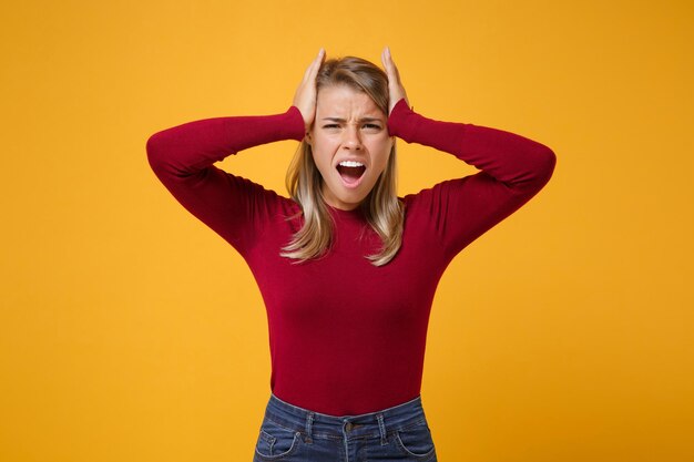 Irritated young blonde woman girl in casual clothes posing isolated on yellow orange background studio portrait. People emotions lifestyle concept. Mock up copy space. Screaming, put hands on head.