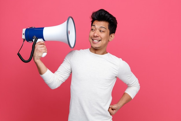 Irritated young man keeping hand on waist holding and looking at speaker 