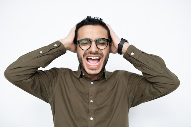 Irritated young mixed-race businessman in eyeglasses keeping his hands on head while screaming in isolation