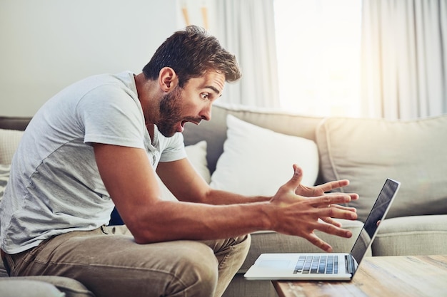 Is your wireless device causing you issues Shot of a frustrated young man looking at his laptop surprised while sitting on the couch at home