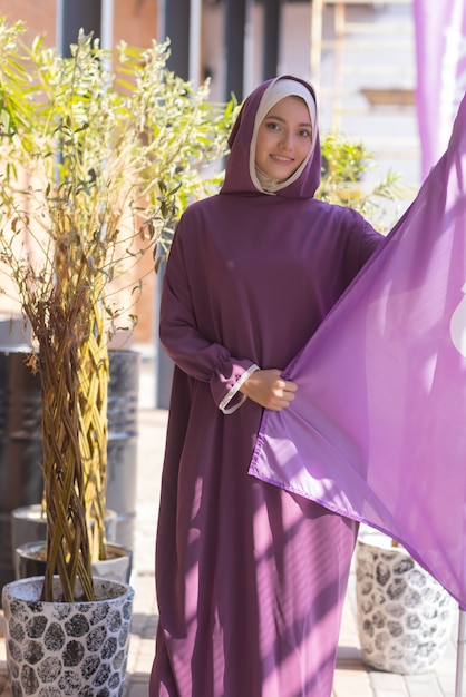 Islamic beautiful woman in a muslim dress standing on a summer park street background forest autumn ...