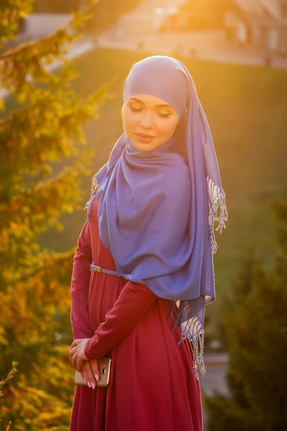 Islamic beautiful woman in a Muslim virgin dress standing on a summer park street background forest autumn trees