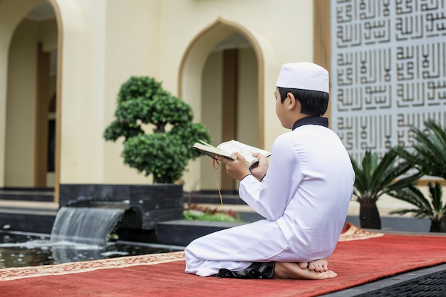 An Islamic boarding school student kneeling while reading the Quran in the courtyard of the mosque