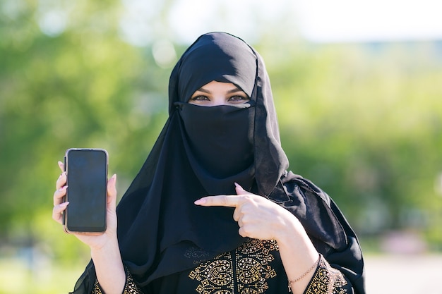 イスラム教徒のイスラム教徒の女性は彼女の手で現代の携帯電話を持っています