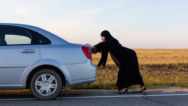 An Islamic woman is pushing a car along the road