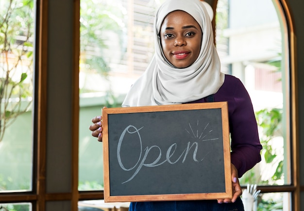 笑顔で黒板を持っているイスラムの女性の中小企業の所有者