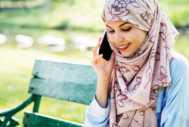 Islamic woman using mobile phone with smiling at park