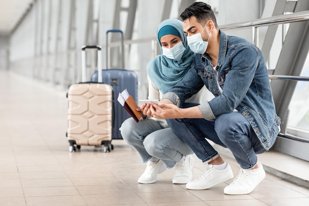 Islamitisch stel dat maskers draagt met smartphone tijdens het wachten op de vlucht op de luchthaven