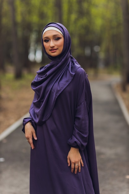 Islamitische mooie vrouw in een moslim jurk staande op een zomer park straat achtergrond bos herfst bomen. wereld hijab dag.