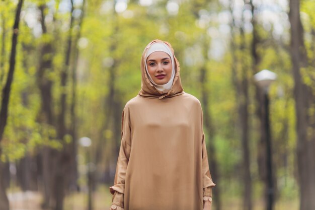 Islamitische mooie vrouw in een moslim jurk staande op een zomer park straat achtergrond bos herfst bomen