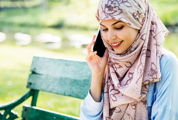 Islamitische vrouw die mobiele telefoon met het glimlachen bij park met behulp van