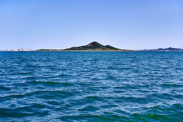 Island near La Manga del Mar Menor seen from inside the sea on a sunny day with a clear blue sky