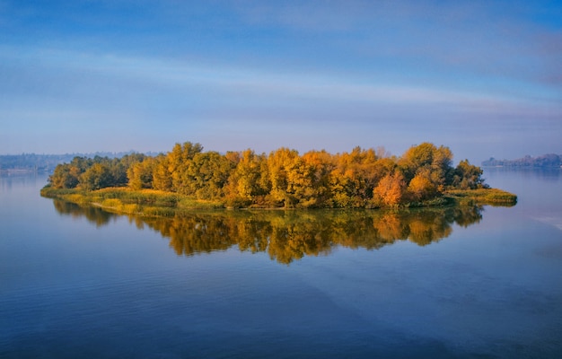 Island with yellow deciduous forest on a wide river