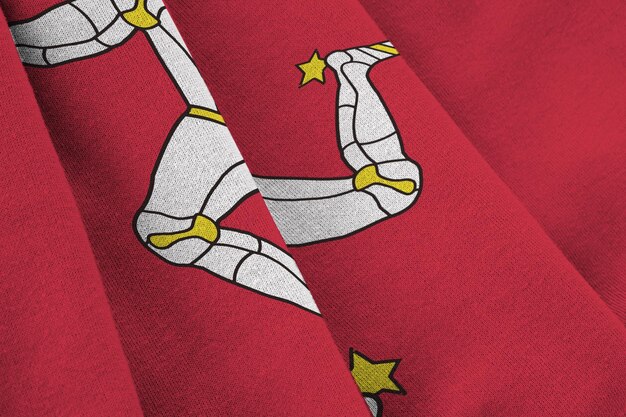 Isle of Man flag with big folds waving close up under the studio light indoors The official symbols and colors in banner