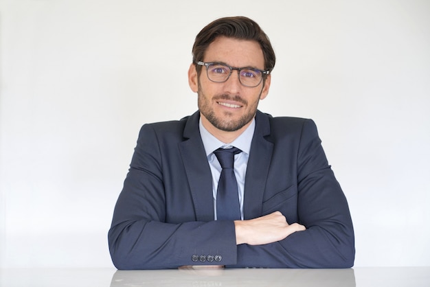 Isolated attractive businessman sitting at desk in suit with arms crossed