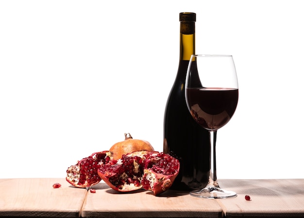 Isolated burgundy red wine bottle, wine glass and juicy pomegranate