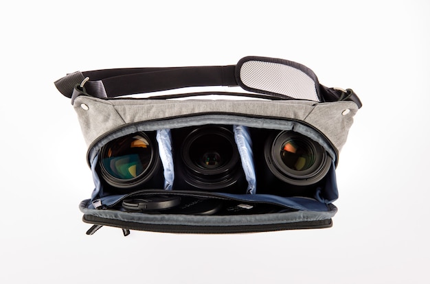 Isolated close up studio shot of small photographer modern fashionable gray shockproof waist bag soft compartment fanny pack carry digital dslr camera len and smartphone inside on white background.