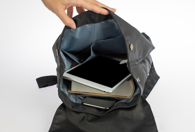 Isolated closeup studio shot of female hand open canvas fabric urban trendy gray crossbody bag with touchscreen tablet textbook and smartphone inside compartment pocket in front white background.