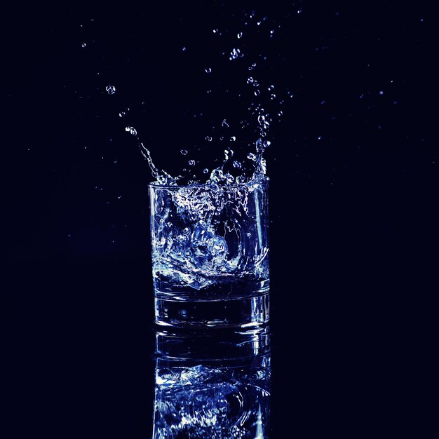 Isolated cold water in a glass with splash and cubes of ice on black background brandy in a glass