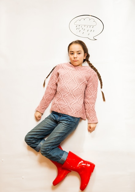 Isolated conceptual shot of sad girl in rubber boots standing under rainy cloud