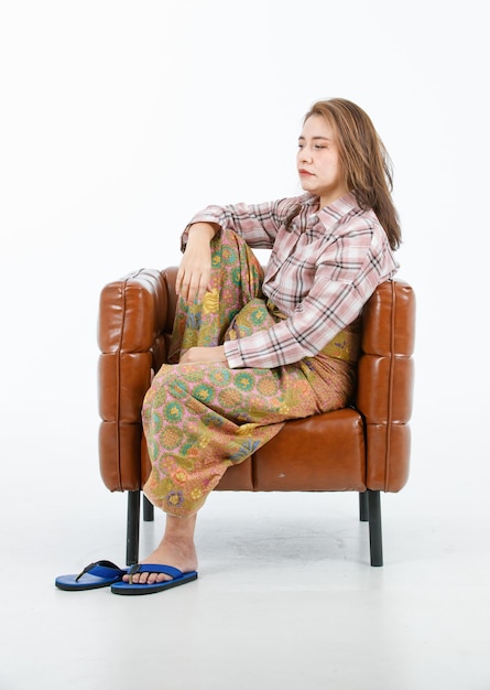 Isolated cutout full body studio shot of Asian poor unhappy upset stressed depressed female model in casual plaid long sleeves shirt sarong sitting brown leather armchair on white background