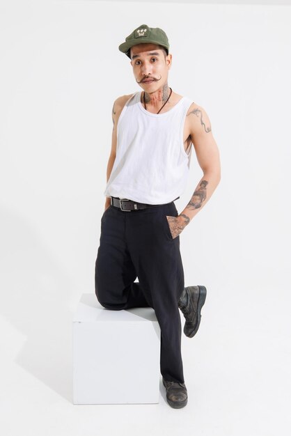 Foto taglio isolato girato in studio vintage asiatico baffi di classe con collo braccia mani tatuaggi modello di moda maschile in casual camicia senza maniche cappello stivali in posa in piedi su sfondo bianco