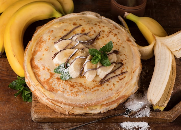 Isolated desert - stack of pancake with chocolate spread and banana on a wooden table