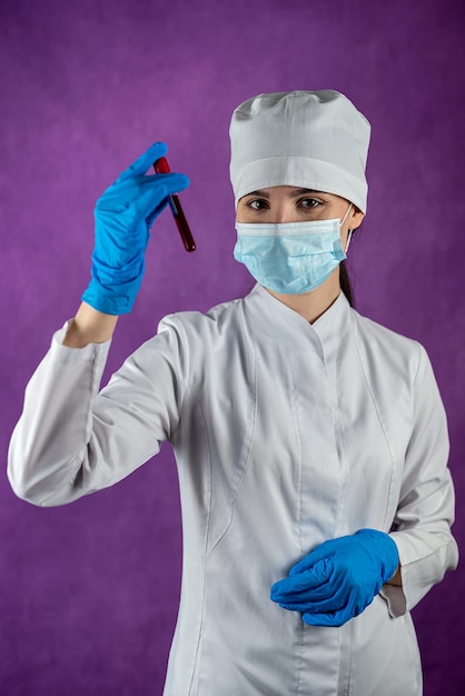 Foto medico femminile isolato in maschera medica e guanti blu che tengono una provetta con campione di sangue per il test del coronavirus su sfondo semplice malattia respiratoria concetto di medicina